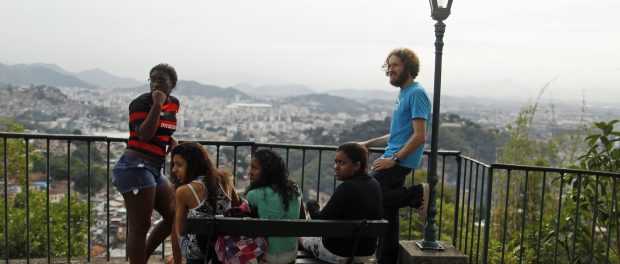 Músico britânico Tom Ashe passa tempo com seus alunos perto da casa que aluga na comunidade Pereira da Silva no Rio de Janeiro. Para muitos gringos de baixa renda, as favelas são os únicos lares a preços acessíveis enquanto o restante do mercado imobiliário está em alta. (Pilar Olivares/Reuters)
