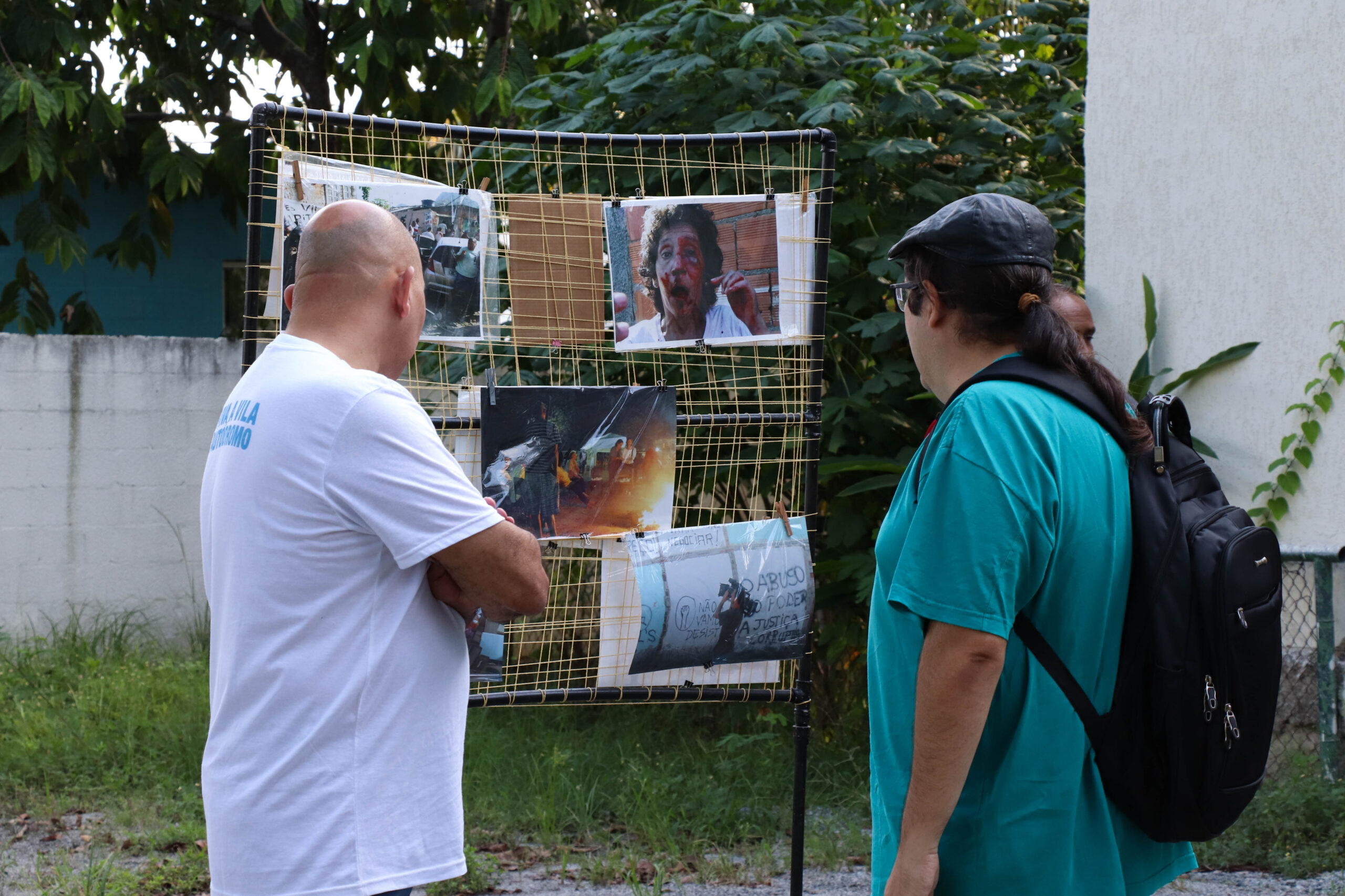 Visitantes, entre eles o vereador Tarcísio Motta, observam fotos do processo violento de remoção da Vila Autódromo coladas em um suporte em formato de rede no Museu das Remoções. Foto: Alexandre Cerqueira