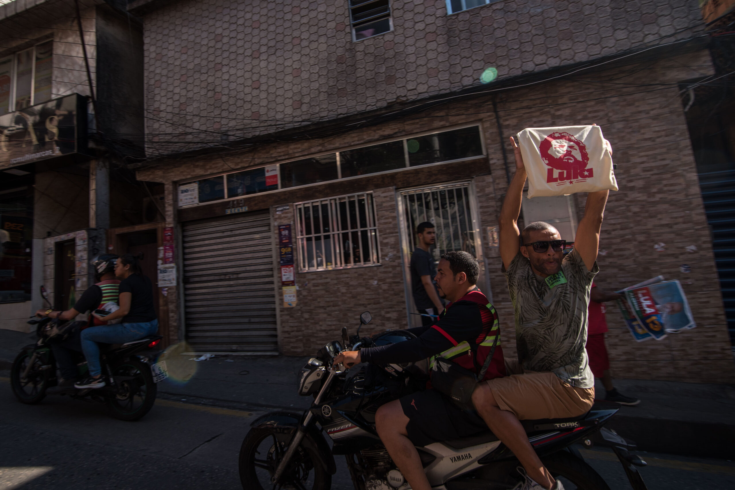 Passageiro de uma moto, ao passar pela Caminhada Rocinha com Lula, mostra uma bolsa estampada com a cara de Lula, em apoio à caminhada e à candidatura do petista. Foto: Bárbara Dias/RioOnWatch