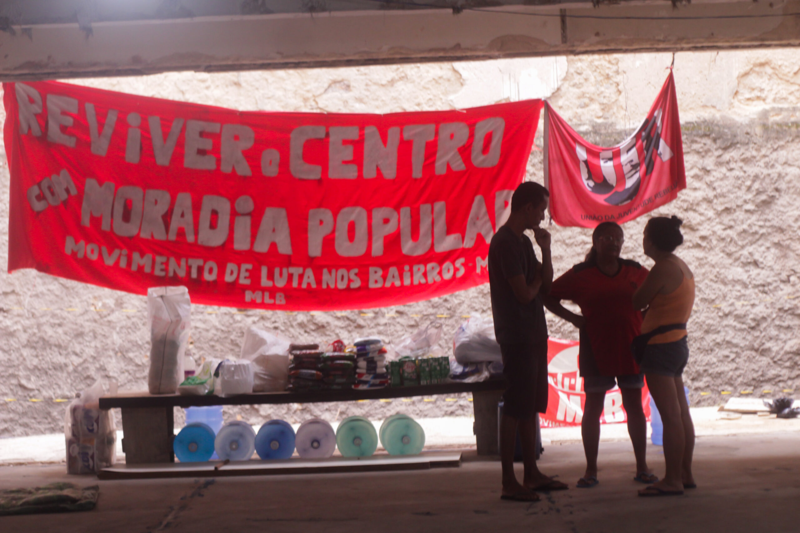 Moradores da Ocupação Luiz Gama em frente a uma faixa do Movimento de Luta nos Bairros, Vilas e Favelas (MLB). Foto: Vinícius Ribeiro