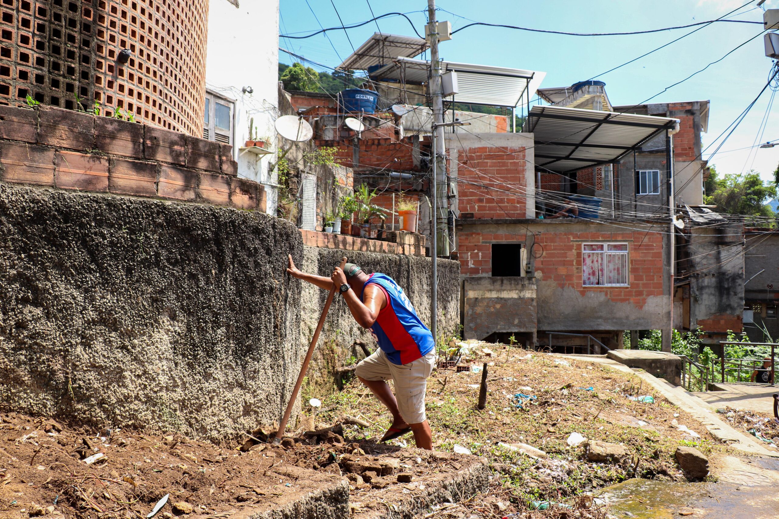 Um morador trabalha na limpeza do canteiro externo da horta comunitária. Foto: Alexandre Cerqueira