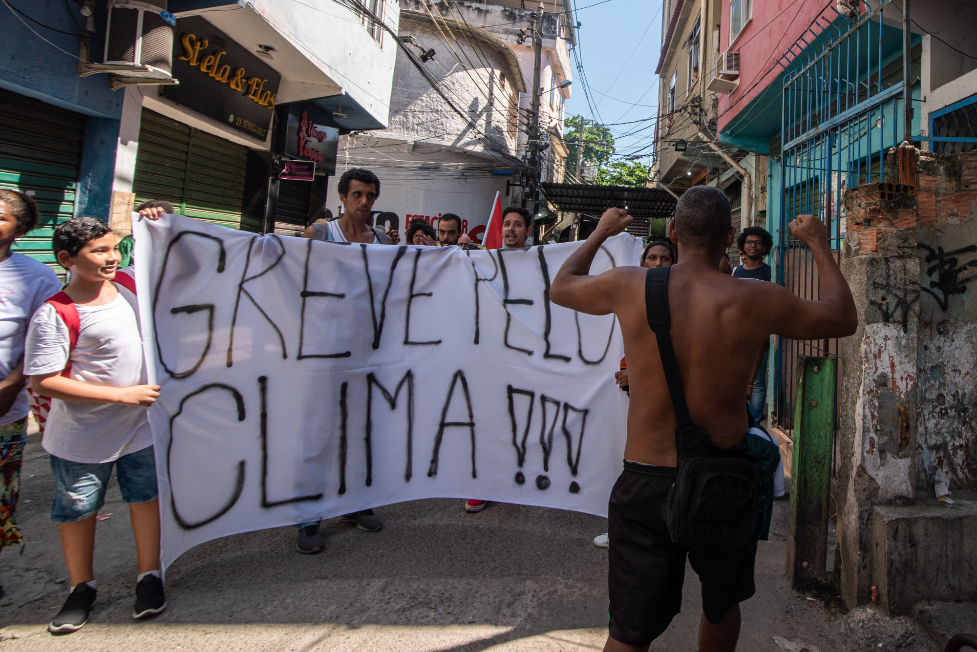 Morador do Jacarezinho, sem camisa devido ao forte calor, ergue os punhos cerrados em apoio à Greve Global pelo Clima em sua comunidade. Foto: Bárbara Dias