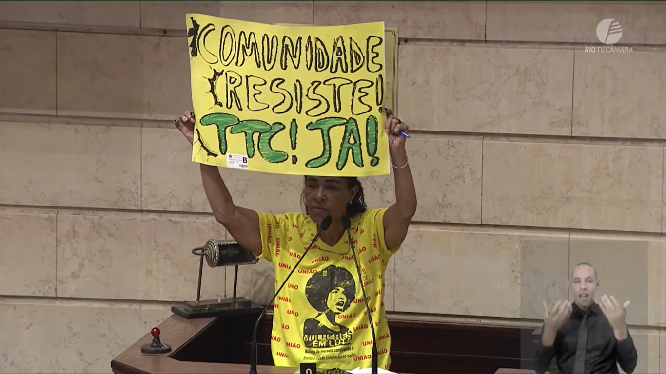 Jurema Constâncio, moradora da Cooperativa Shangri-lá, levanta cartaz 'Comunidade resiste! TTC Já!' durante sua fala na audiência pública sobre o Plano Diretor.