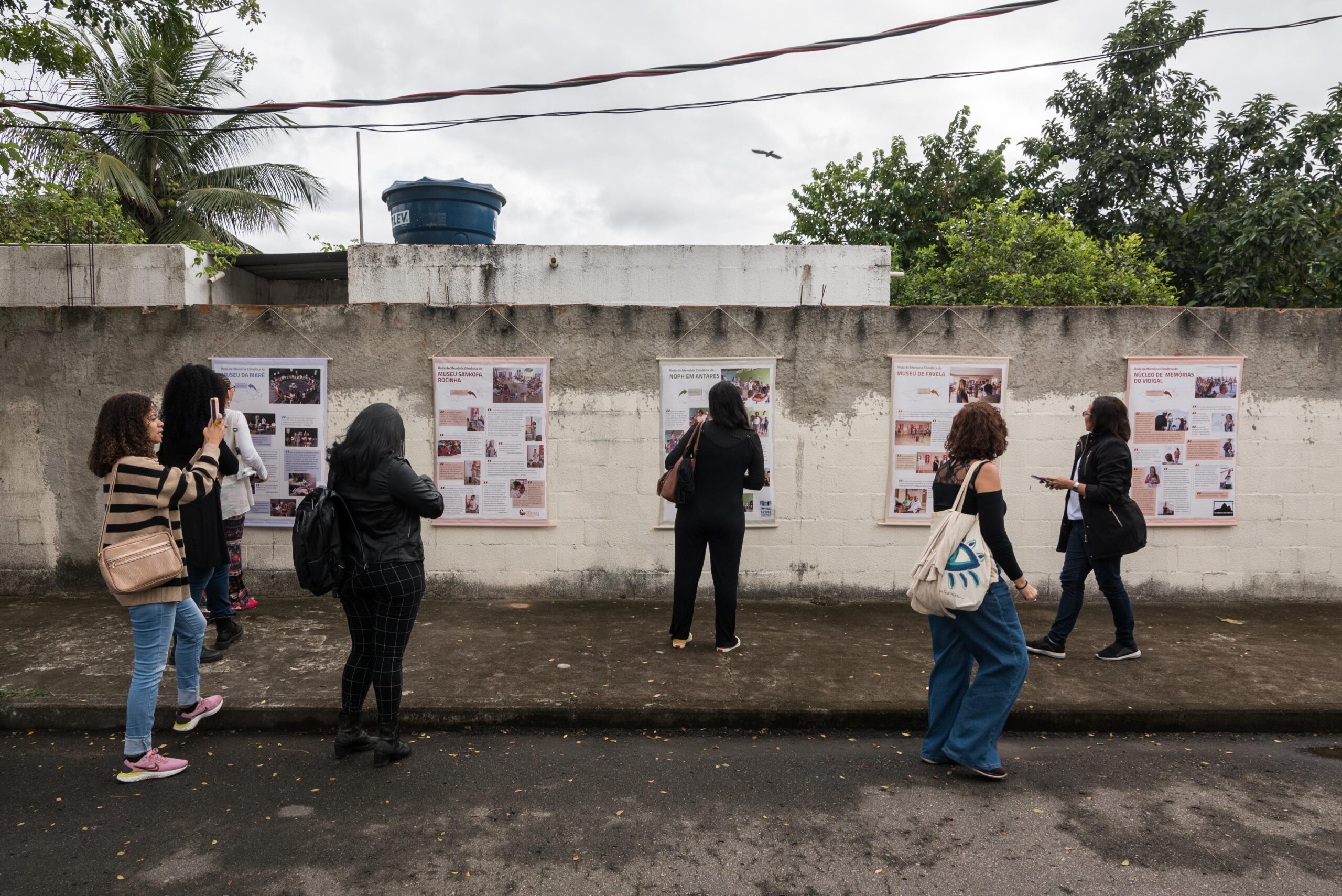 Visitantes observam os banners com o resumo de cada atividade que aconteceu nas cinco comunidades participantes da Exposição de Memória Climática das Favelas. Foto: Bárbara Dias