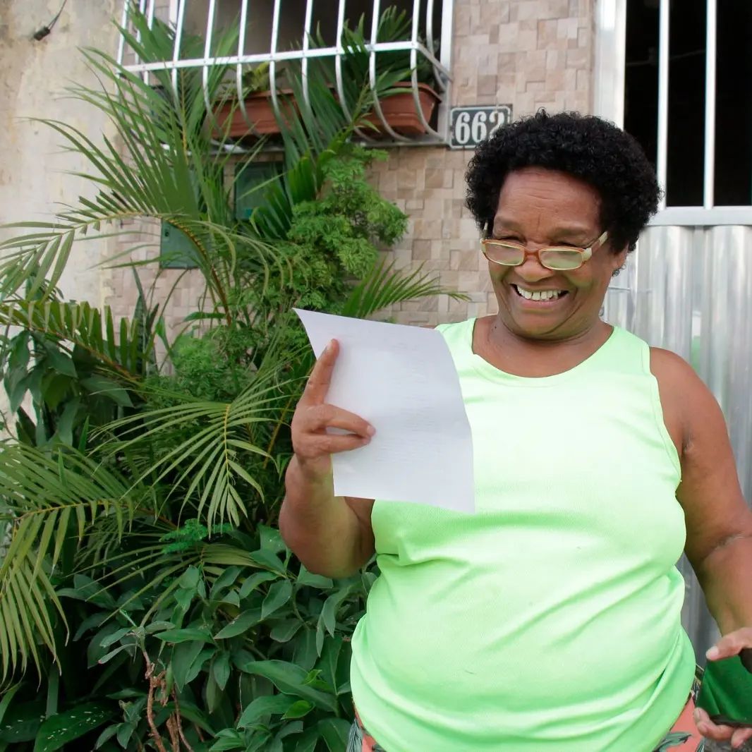 No primeiro desfile do Bloco Se Benze Que Dá em 2024, moradora lê a letra do samba do bloco e sorri. Foto: Divulgação Redes Sociais Bloco Se Benze Que Dá