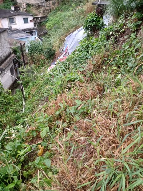 Lucas relata que o barranco da base de uma casa cedeu, atingindo a casa abaixo, interditando o caminho por meses. Ele conta que a casa branca abaixo tem uma marcação na parede, sendo altura que o barro chegou. Foto: Lucas Prates/Projeto Social Família 18