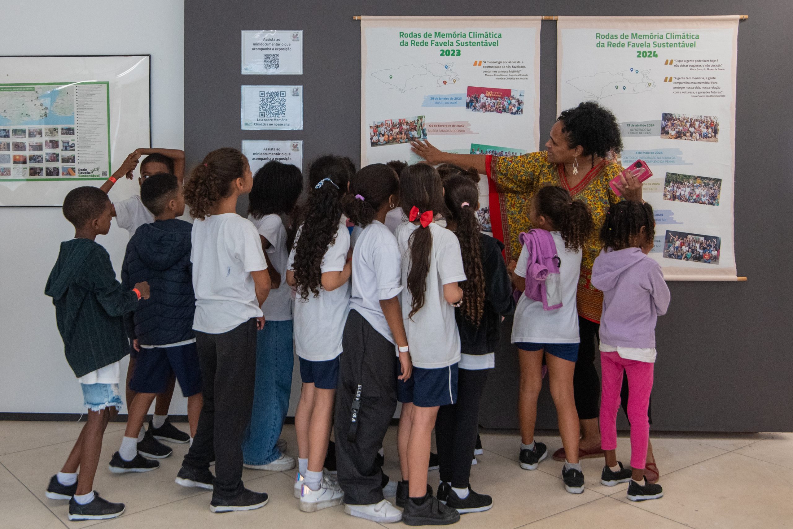 Márcia Souza (à direita) guia jovens estudantes da Escola Municipal Presidente João Goulart na Exposição Memórias Climáticas das Favelas no Museu das Favelas. Foto: Bárbara Dias Márcia Souza (à direita) guia jovens estudantes da Escola Municipal Presidente João Goulart na Exposição Memórias Climáticas das Favelas no Museu das Favelas. Foto: Bárbara Dias