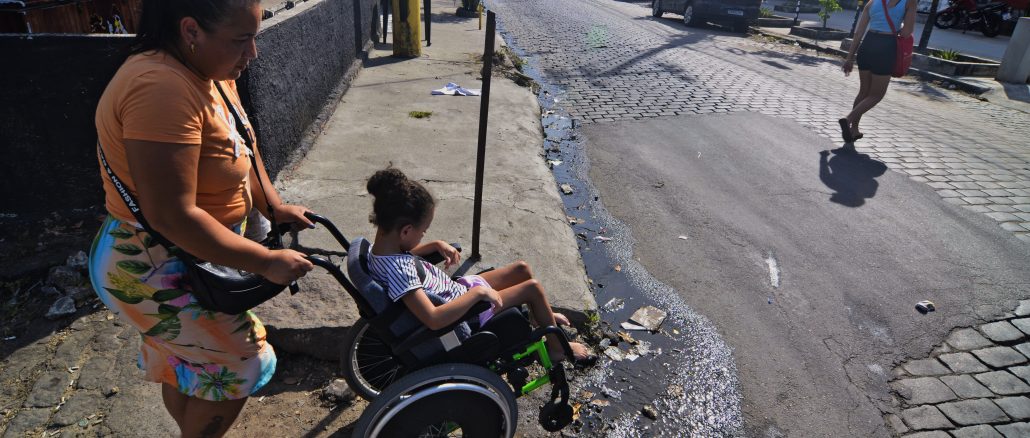 Ana Raquel, 37 anos, subindo o morro do Timbau com Eloah para chegar em casa, é obrigada a passar com sua filha na cadeira de rodas por esgoto a céu aberto. Foto: Ramon Vellasco