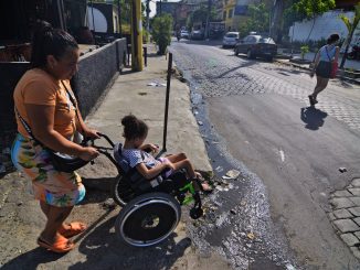 Ana Raquel, 37 anos, subindo o morro do Timbau com Eloah para chegar em casa, é obrigada a passar com sua filha na cadeira de rodas por esgoto a céu aberto. Foto: Ramon Vellasco